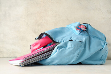 Blue backpack with school supplies on table against white grunge wall