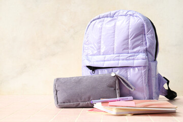 Lilac backpack with school supplies on table against white grunge wall