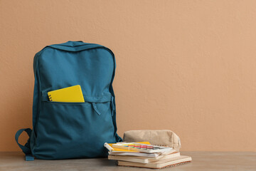Blue backpack with notebooks, palette and pencil case on table against beige wall