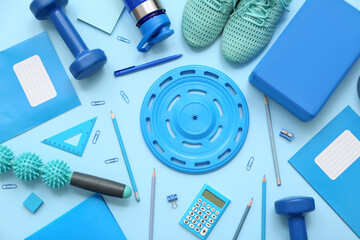 Dumbbells, frisbee, sneakers, yoga block, massage roller stick and different stationery on blue...
