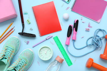 Sneakers, jumping rope, golf ball, golf club, dumbbells, alarm clock and different stationery on blue background