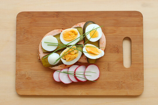 Ein Brot mit Wurst, Ei, Gurken, Radieschen und Schnittlauch auf einem Holzbrett