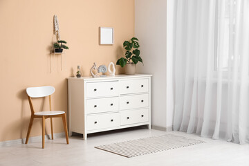 White chest of drawers with houseplant and chair near beige wall in room