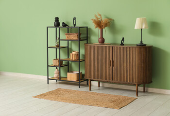 Dark wooden chest of drawers with lamp and vase of pampas grass near shelving unit in room