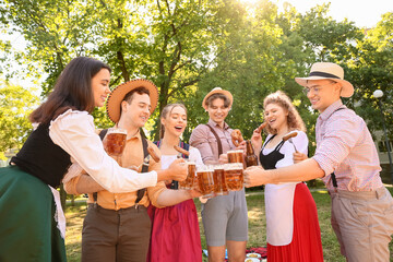 Young people in traditional German clothes with beer and sausages celebrating Octoberfest outdoors