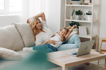 Mother and daughter bonding time on the couch with a laptop, surrounded by a cozy bookshelf backdrop