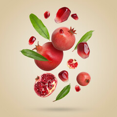 Fresh pomegranates, seeds and leaves in air on beige background