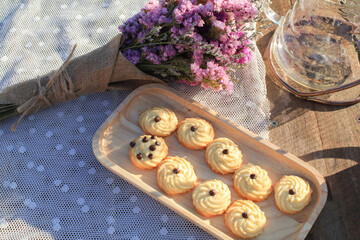 Butter cookie on wooden tray eating coffee under morning sunlight and purple flower on table. Breakfast with nature.