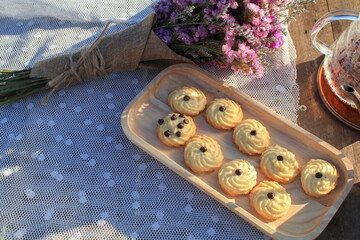 Butter cookie on wooden tray eating coffee under morning sunlight and purple flower on table. Breakfast with nature.