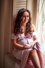 Portrait of a beautiful young pregnant woman sitting on the windowsill