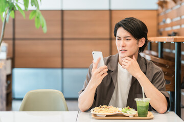 カフェ・家などでスマホを使う若いアジア人男性（困る・悩む・考える・悩み・失敗・ショック）
