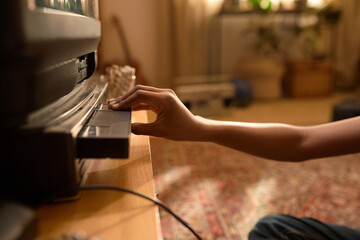 Close-up of hand inserting VHS tape into old-school VCR player standing on wooden table in cozy living room with retro design