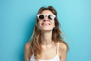 Fototapeta premium Cheerful young woman in sunglasses against blue background