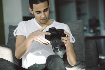 Young photographer sitting on couch reviewing photos on camera