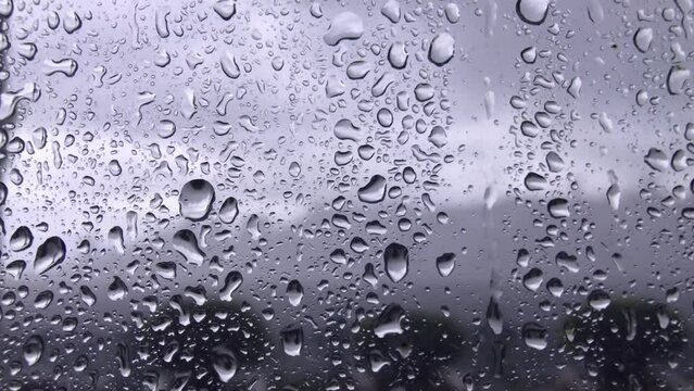 Rainy day water drops fall down on window glass. Raindrops dripping down the glass. Rain drop on glass as footage background. Closeup 4k footage of rainy texture of wet from raindrops glass of window.