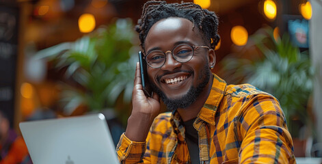 Smiling man talking on phone while working on laptop at office desk professional portrait bright light