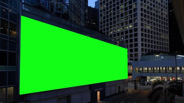 Night city large billboard with a green screen for advertising on the building wall.
