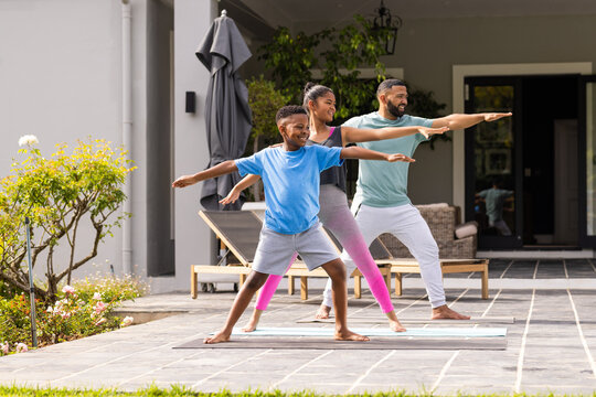 African American father practices yoga outdoors with his son and daughter