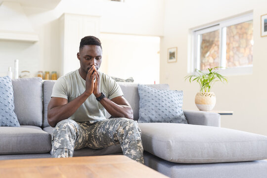 Troubled african american male soldier sitting on couch at home thinking, copy space