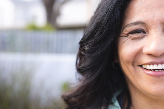 Half portrait of happy senior biracial woman with long black hair smiling outdoors, copy space