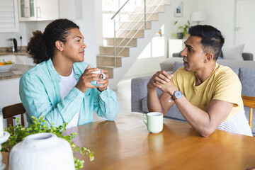Young biracial man and Middle Eastern man, a gay couple, share a conversation over coffee at home
