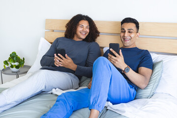 Gay biracial couple enjoys leisure time in bedroom, with copy space