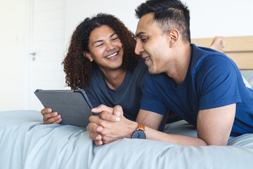 Gay biracial couple enjoys a tablet in bed at home