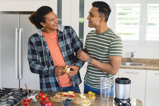 Biracial gay couple and Middle Eastern gay couple prepare food together at home