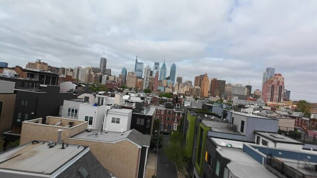 Modern row houses near downtown Philadelphia skyline. Aerial FPV drone shot fast and low over rooftops in urban USA city.