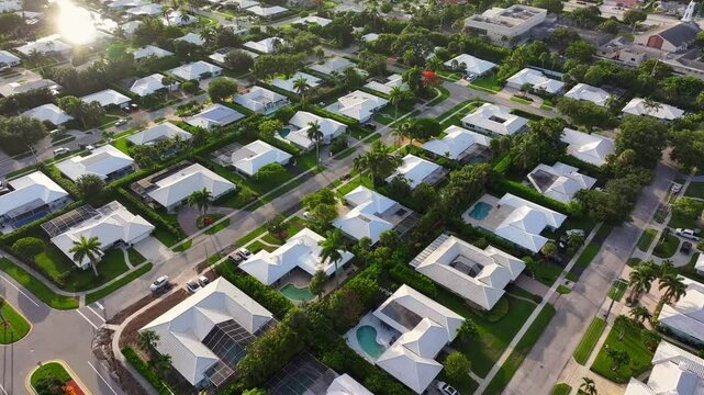 Expansive residential homes in a gated golf community in South Florida. American dream. Florida real estate development. Golden hour light drone shot. White roofs, green lawns and palm trees.