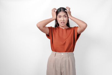 Stressed young Asian woman in a brown shirt and taupe pants is holding her head in her hands...