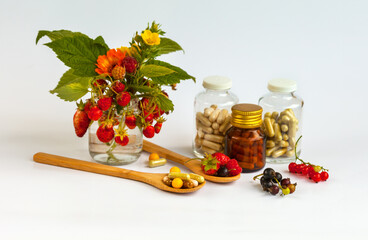 Natural vitamins in currants, raspberries, strawberries next to dietary supplements in form of capsules in wooden spoons and glass medicine bottles on white background. Concept care of health 