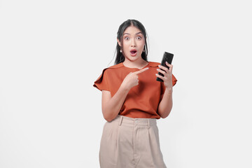 Fototapeta premium Shocked young Asian woman in brown shirt pointing to the cellphone she holds.