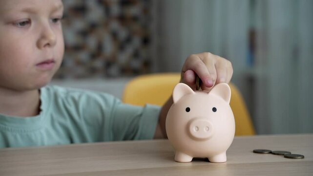 A young boy sits at a table, intently dropping coins into his piggy bank. He's saving up for something special.