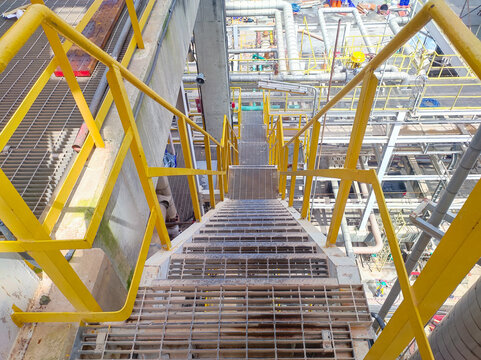 grating stairs with yellow handrail in factory area