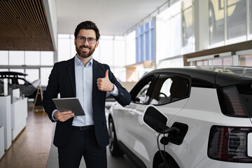 Dealer in showroom showcasing new electric car to customer giving thumbs up. Modern car dealership interior. Salesman holding tablet representing eco-friendly vehicle electric mobility sustainability.