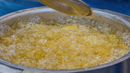 Potatoes in boiling oil. Close-up of potatoes frying in hot oil. Potato pieces surrounded by bubbles from boiling oil during cooking. French fries. Selective focus.