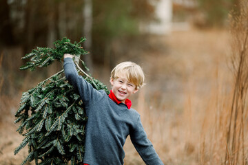 Boy carrying a Christmas tree outdoors