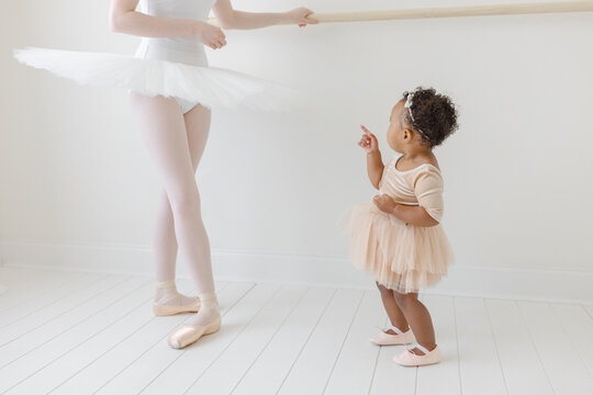 mixed race baby in tutu admires ballerina in ballet studio