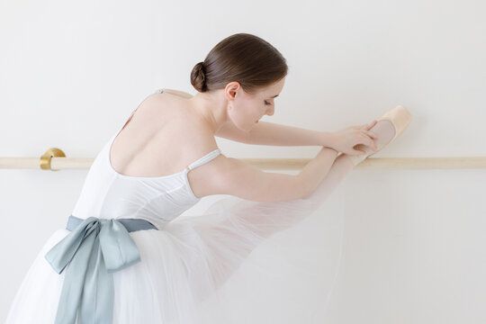 ballerina stretches on ballet barre in white tutu