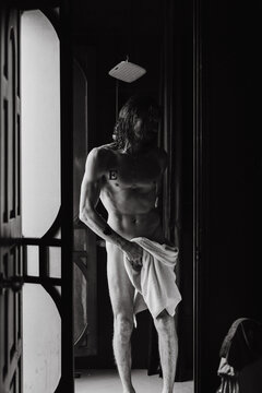 Young naked man with long hair in the shower. Black and white portrait