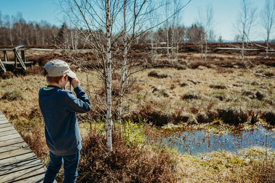 Boy watching frogs through binoculars in a high moor on a clear day