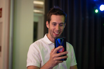 Portrait of a young guy recording and taking photos with his cell phone at the dance after the...