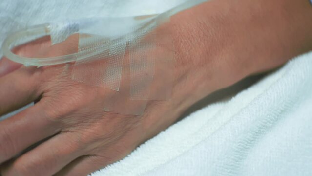 A close-up of a patient resting in a hospital bed with an IV drip in hand, showcasing healthcare and hospital care details.