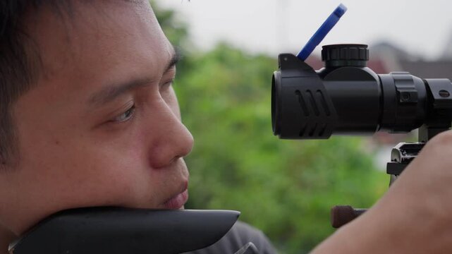 Asian Marksman Opens Scope Of PCP Air Rifle And Aims On Target. closeup, side view