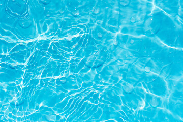 Blue water with ripples on the surface. Defocus blurred transparent blue colored clear calm water surface texture with splashes and bubbles. Water waves with shining pattern texture background.