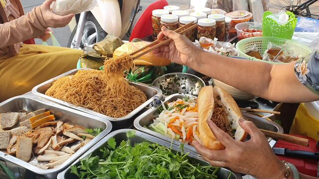 Woman making vegan Vietnamese bread or banh mi, popular Vietnam street food, raw material in tray, hands stuffing ingredient into sandwich to make delicious meal