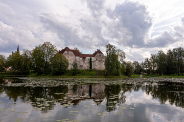 Obraz premium Historic Stone Castle Reflecting in Tranquil Latvian Lake on Cloudy Summer Day