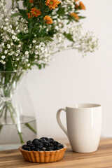 berry tartlet made from shortcrust pastry, white mug and a bouquet of flowers in the background. Summer morning
