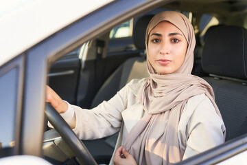 A woman wearing a hijab is driving a car